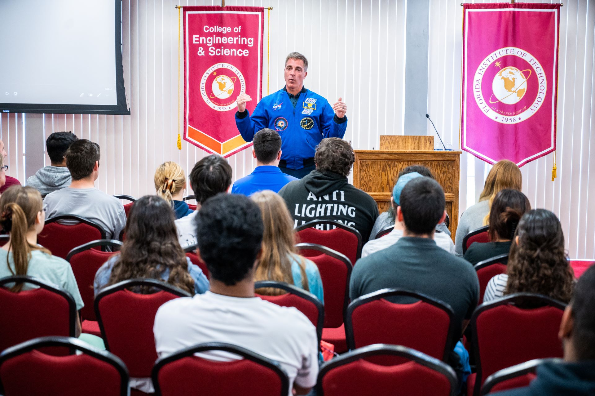 An instructor in an astronaut suit teaching in a classroom full of students